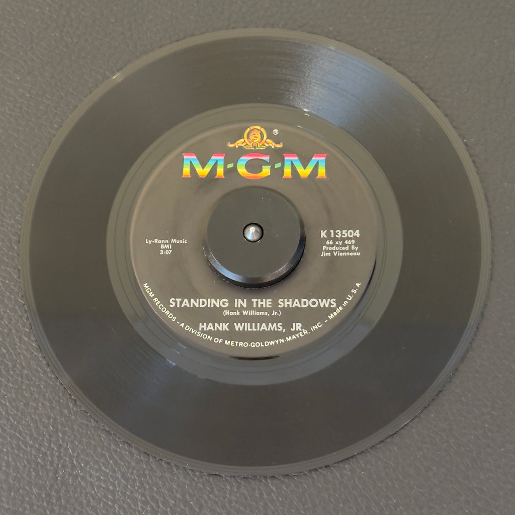 7" vinyl record by Williams Jr, Hank featuring "Standing In The Shadows/It's Written All Over Your Face", released on MGM Records (K13504), in VG+ (Very Good Plus) condition, classic analog collectable for turntable playback. Original MGM sleeve included.