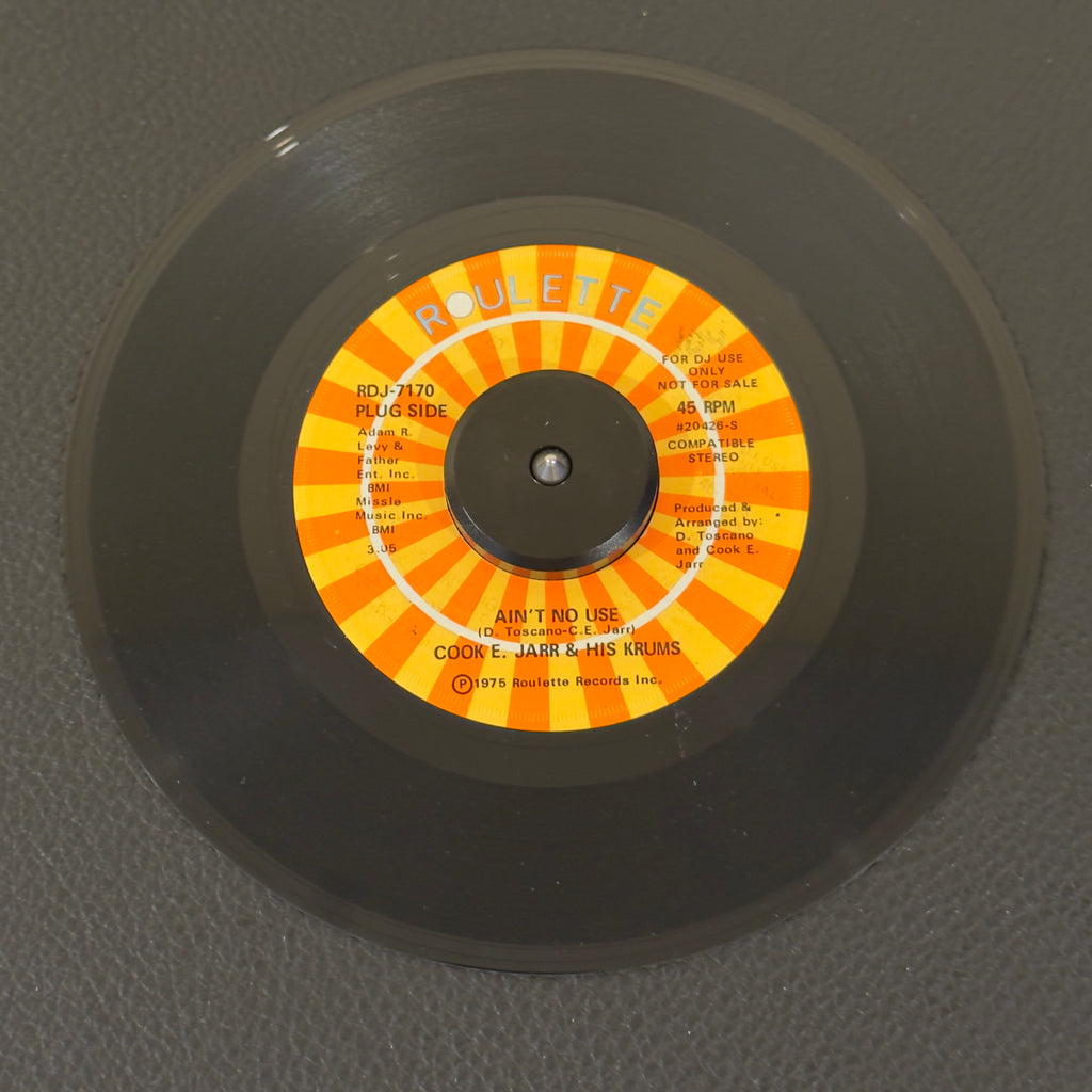 7" vinyl record by Jarr, Cook E. & His Crumbs featuring "Ain't No Use/(Part 2) (Instrumental)", released on Roulette (RDJ-7170), in NM (Near Mint) condition, classic analog collectable for turntable playback. Promo copy with original sleeve!  Before cementing his status as an iconic, Vegas entertainment legend, Cook E. Jarr cut some of the nastiest East Coast funk-crossover of the mid-70s. WOL
