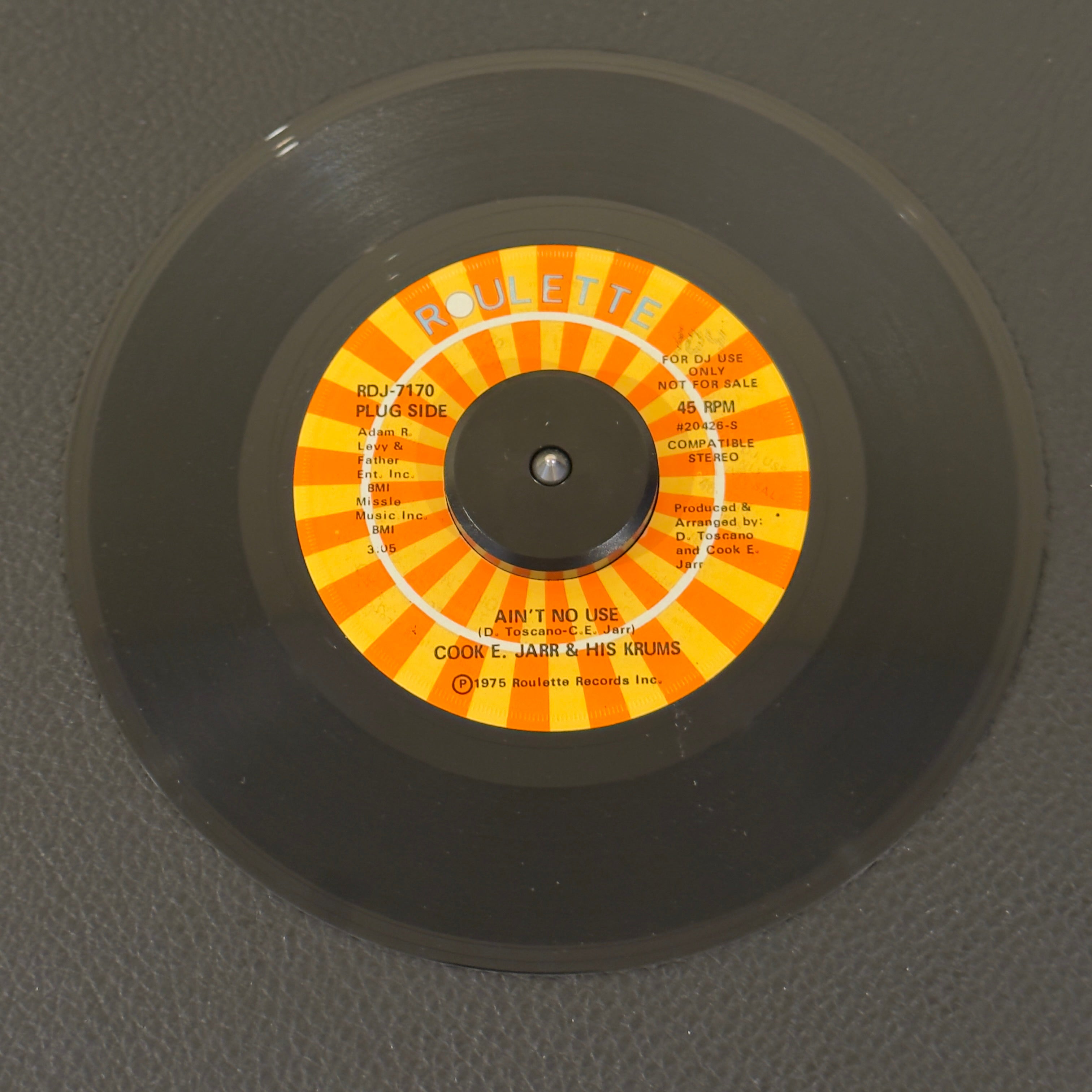 7" vinyl record by Jarr, Cook E. & His Crumbs featuring "Ain't No Use/(Part 2) (Instrumental)", released on Roulette (RDJ-7170), in NM (Near Mint) condition, classic analog collectable for turntable playback. Promo copy with original sleeve!  Before cementing his status as an iconic, Vegas entertainment legend, Cook E. Jarr cut some of the nastiest East Coast funk-crossover of the mid-70s. WOL
