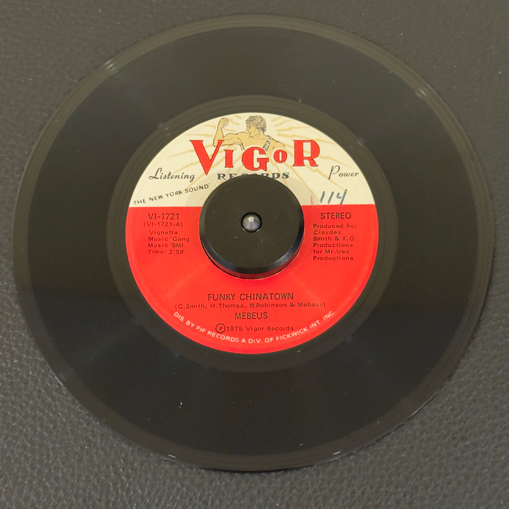 7" vinyl record by Mebeus featuring "Funky Chinatown/Jackie", released on Vigor Records (VI-1721), in NM (Near Mint) condition, classic analog collectable for turntable playback. This rare, 1975 underground synth-and-horn-driven dancefloor mover encapsulates the raw, driving energy of East Coast disco-funk.  Vinyl is NM with writing on both sides of the label.